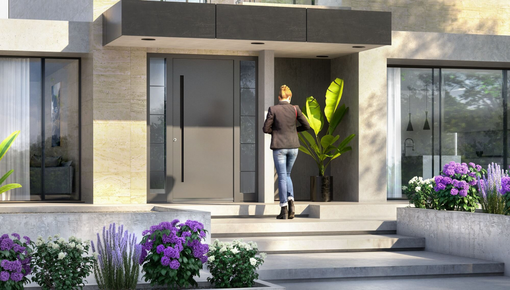 Moderne Aluminium-Eingangstür Inotherm in einem großen Haus mit lila Blumen im Hof und dem Besitzer, der nach Hause kommt.