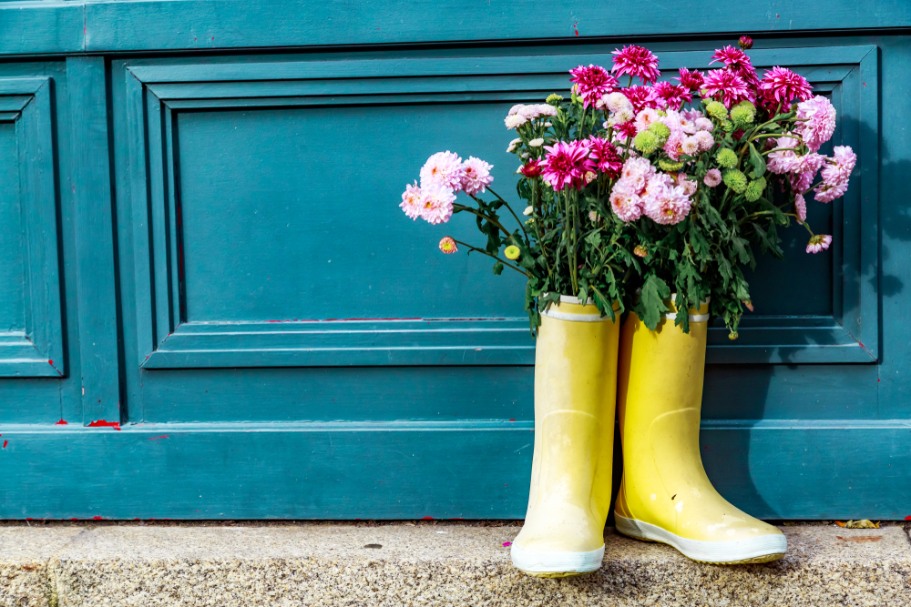 Blaue Haustür, vor der sich gelbe Gummistiefel wie ein Blumentopf für Blumen befinden.