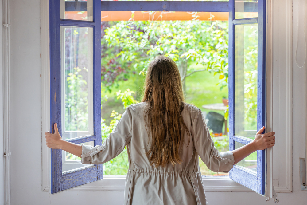 Eine Frau öffnet das Fenster, um frische Luft ins Haus zu lassen.
